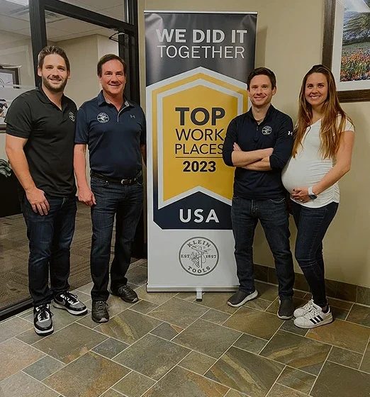 Klein family members standing next to top work places award banner