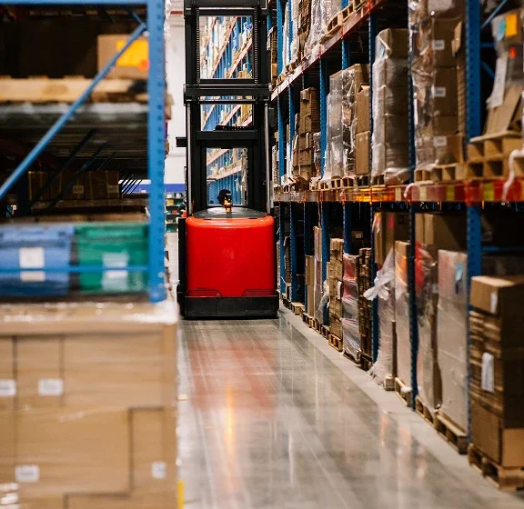 photo of a distribution center aisle with tall shelves on both sides and a forklift in the middle